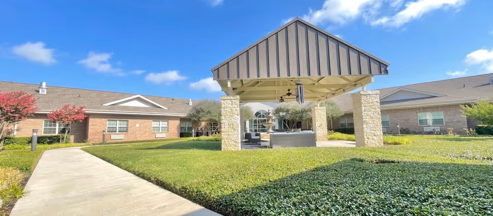 A sunny outdoor seating area with a covered pavilion surrounded by well-maintained gardens at Avir at Killeen.