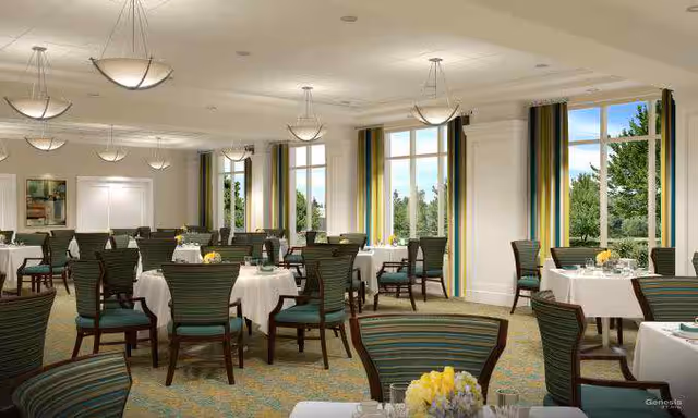 Bright formal dining room with round tables draped in white cloths, green-striped chairs, large windows, and hanging pendant lights.