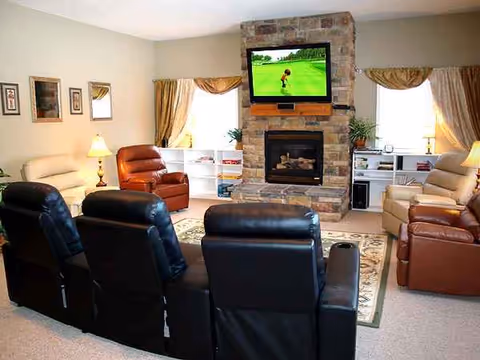 A senior living lounge with recliners, a stone fireplace, and a mounted TV.