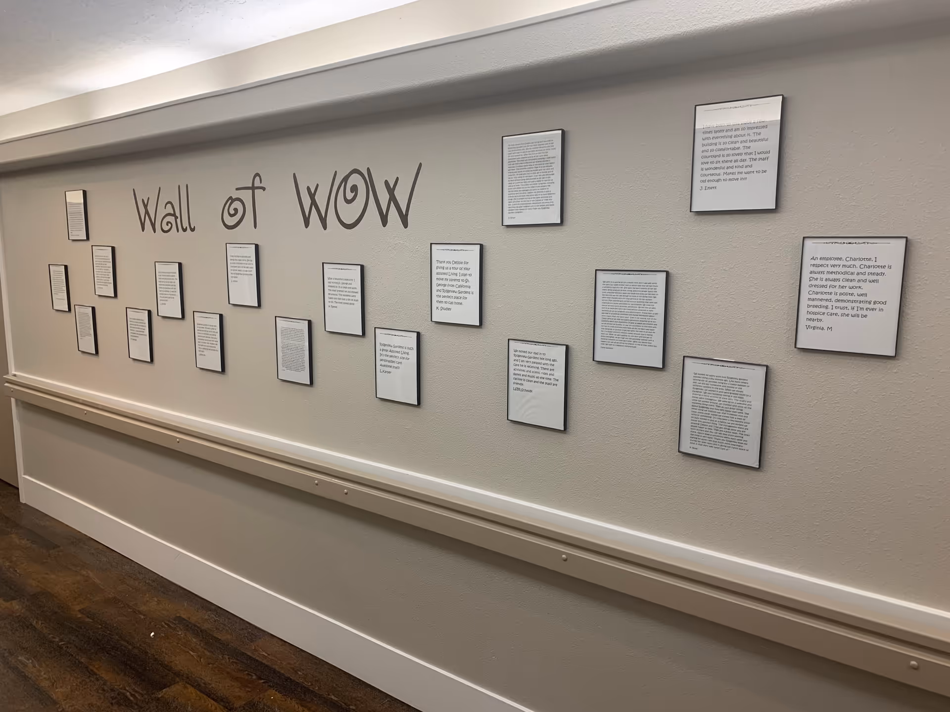 A hallway wall in Ridgeview Gardens Assisted Living labeled 'Wall of WOW' with multiple framed written testimonials or notes displayed in a neat arrangement. The wall is light-colored and the floor has dark wood-like flooring.