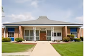 Front exterior view of Lynwood Manor building with a walkway leading to the main entrance, surrounded by green grass and small bushes under a partly cloudy sky.
