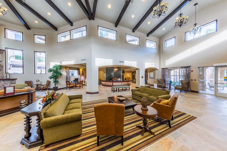 Spacious high-ceilinged senior living lobby with sofas, armchairs, coffee tables, a reception desk and large windows.