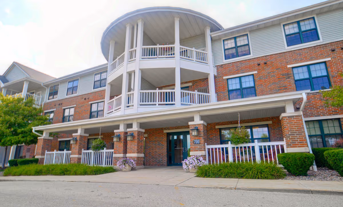 Brick three-story senior living building with covered entrance, round balconies, and landscaped front.