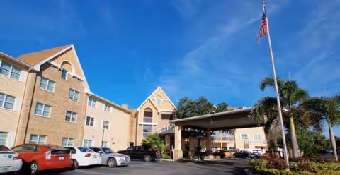 Exterior view of Bayside Terrace senior living with parked cars, entrance canopy, and flag.
