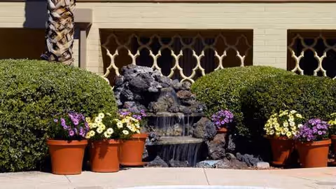 Front exterior of Atria Valley Manor with trimmed hedges, potted flowers, and a small rock fountain.