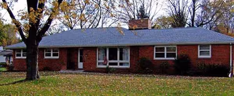 A single-story brick building with a front yard, trees, and a central entrance.