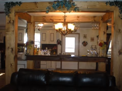 Leather sofa in the foreground facing an open interior with a wooden framed pass-through, chandelier, and a kitchen/bar area beyond.