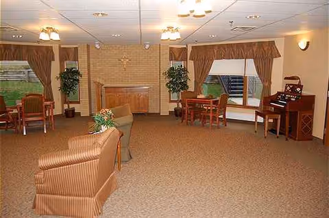 A spacious senior living lounge with plush seating, tables, a piano, and plants.