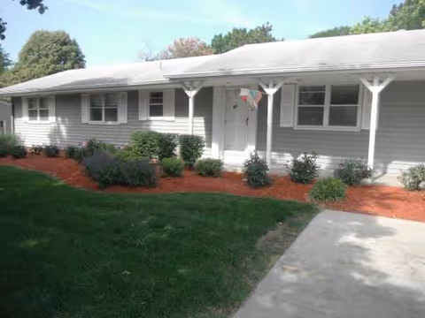 Single-story senior living facility exterior with a covered front porch and shrubs.