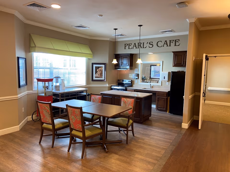 Interior communal dining area and kitchen labeled 'PEARL'S CAFE' with a table and chairs, kitchen island, and appliances.