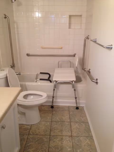Accessible bathroom with a toilet, bathtub fitted with a transfer bench and multiple grab bars.