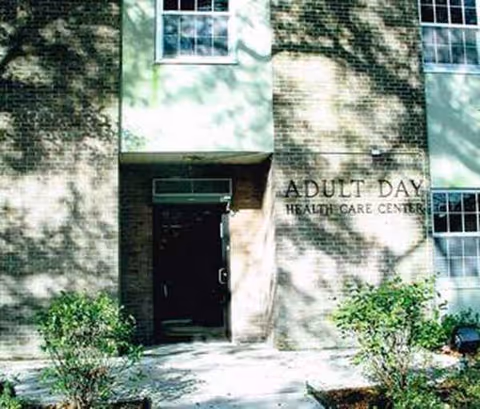 Exterior brick building entrance with Adult Day Health Care Center sign and landscaping.