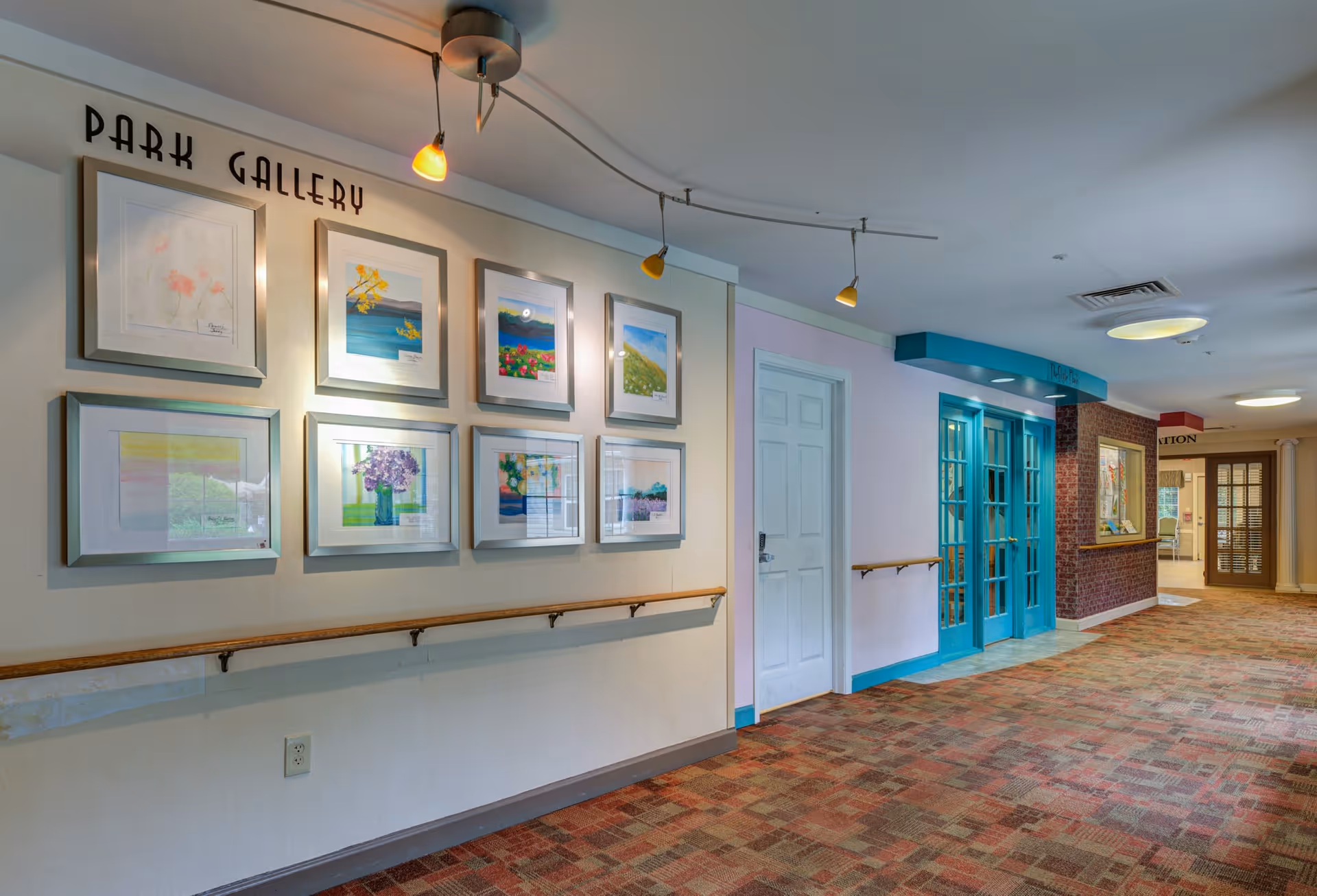 Interior hallway of Arden Courts - ProMedica Memory Care Community (Fair Oaks) featuring a wall labeled 'Park Gallery' with framed artwork, handrails along the walls, a carpeted floor, and a set of blue double doors on the right side.