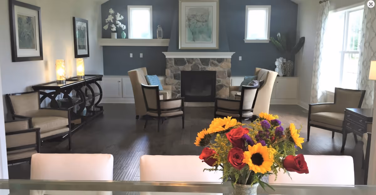 A cozy lobby area featuring a stone fireplace, comfortable seating, and decorative plants. A vibrant flower arrangement is in the foreground, adding color to the space.