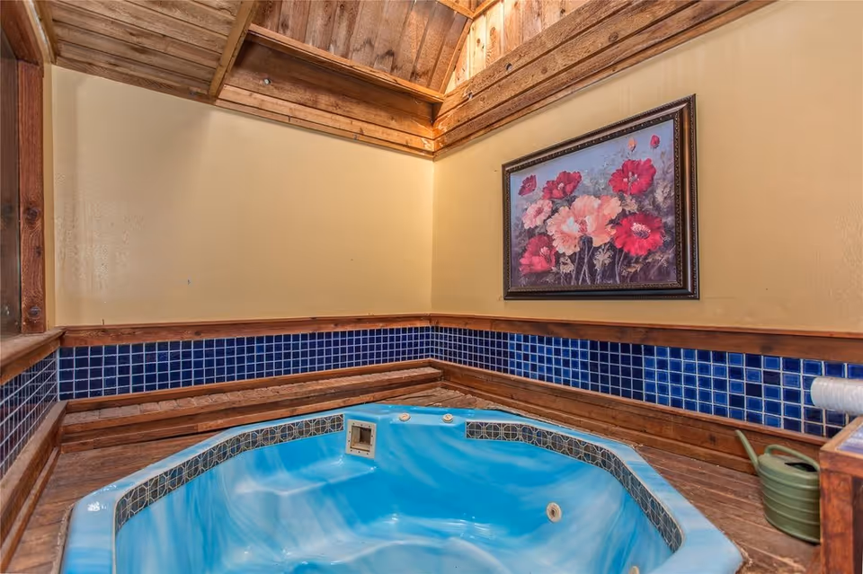 Indoor blue-tiled hot tub/jacuzzi in a wood-trimmed room with a framed floral painting on the wall.