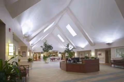 Spacious senior living facility lobby with vaulted ceiling, skylights, reception desk, and seating.