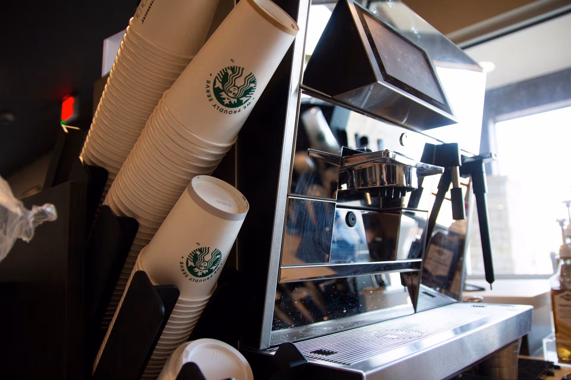 Close-up of a commercial espresso machine beside stacks of Starbucks paper cups and lids at a coffee station.