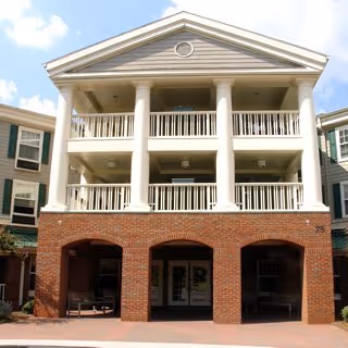 Front facade of a three-story residential building with brick arches on the ground floor and white columns with balconies above.