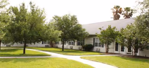 Exterior of WestMark Senior Living with curved walkway, lawn, and trees.