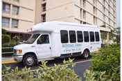 White Jefferson Center shuttle parked beside a multi-story beige senior living building.
