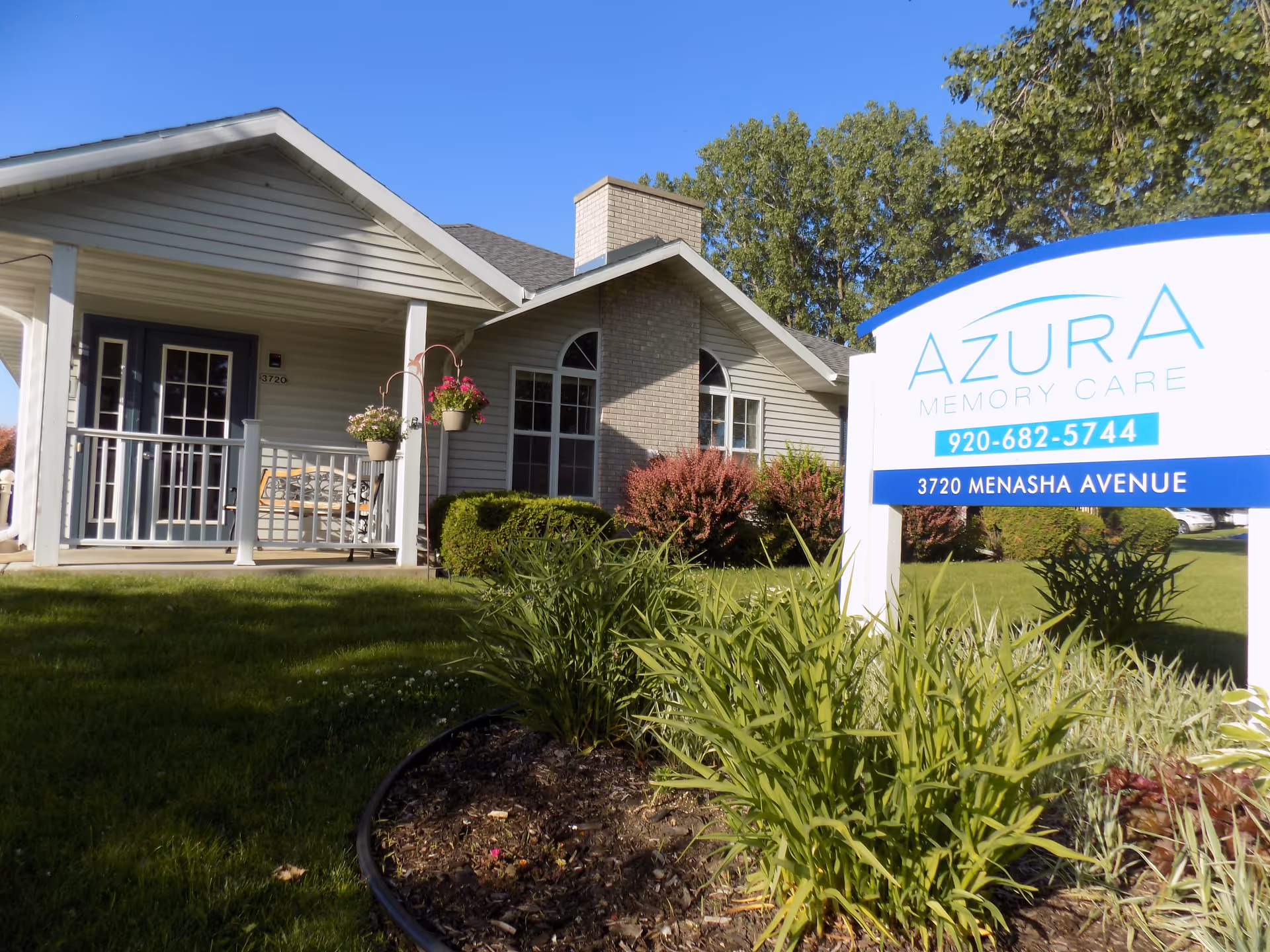 Front exterior of a single-story memory care building with a porch, landscaped lawn, and a large sign reading Azura Memory Care.