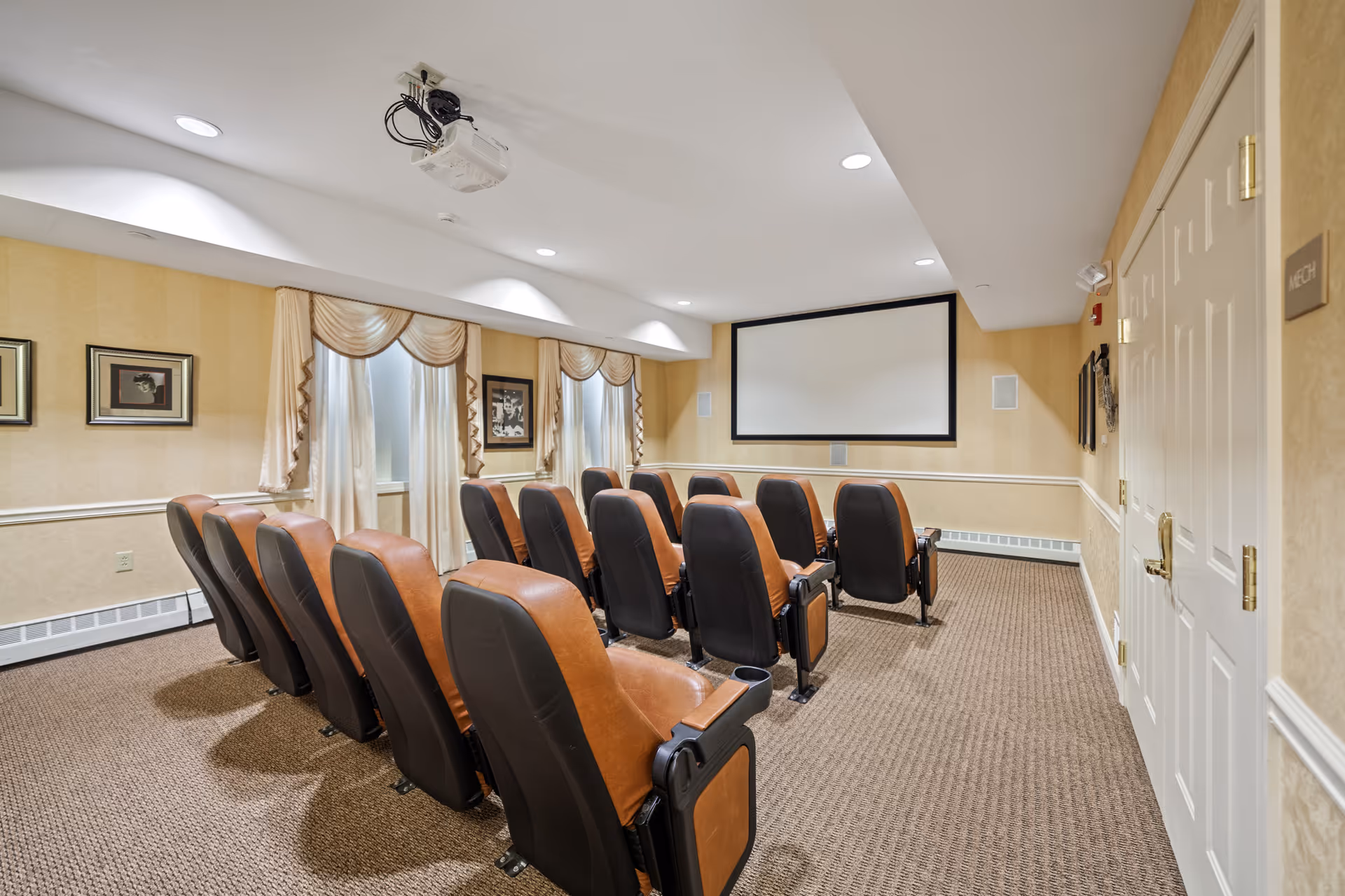 Small private theater room with rows of leather recliner seats facing a projection screen and ceiling-mounted projector.