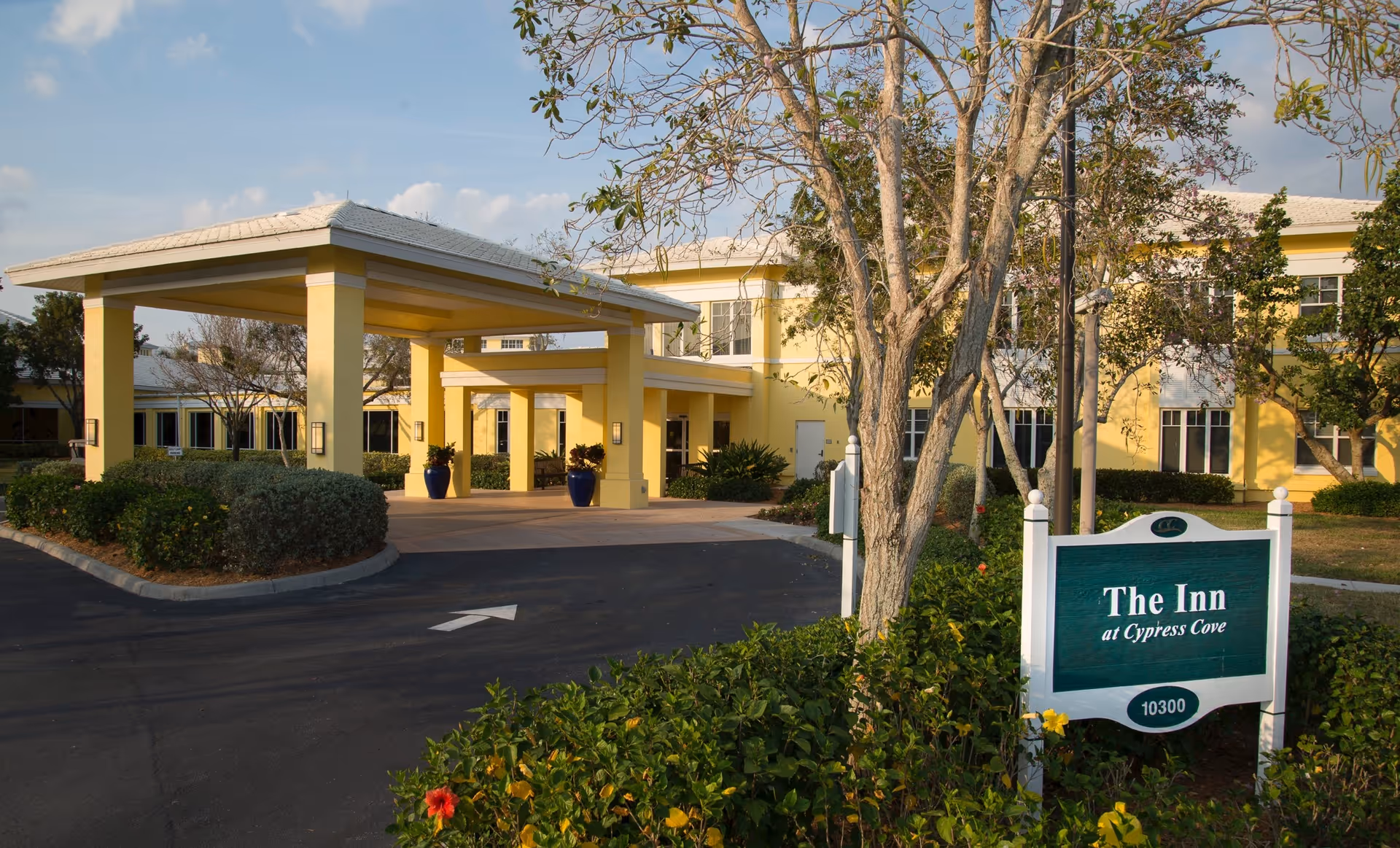 Front entrance of a yellow senior living building with a covered drop-off and a sign reading "The Inn at Cypress Cove".