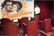 Small screening room with red upholstered seats facing a large 'Casablanca' movie poster and a mannequin in a white jacket near a red curtain.