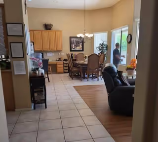 Open-plan interior with a dining table and chairs, kitchen cabinets, a recliner, and a person standing by sliding glass doors.