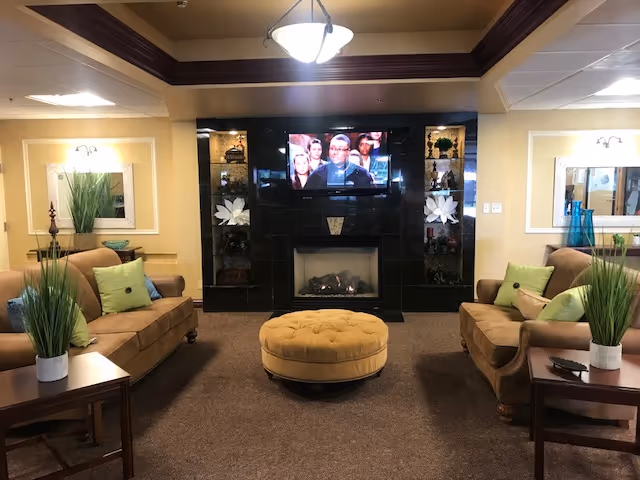 Cozy communal living room with sofas, a round ottoman, fireplace and wall-mounted TV.