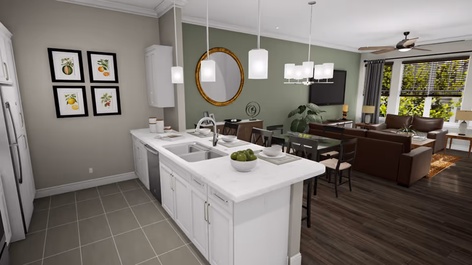 A modern open-concept living space featuring a white kitchen island with a sink and a bowl of green apples, a dining table with chairs, and a living room area with brown leather sofas, a large window with blinds, a ceiling fan, and wall decorations including framed fruit prints and a round mirror.