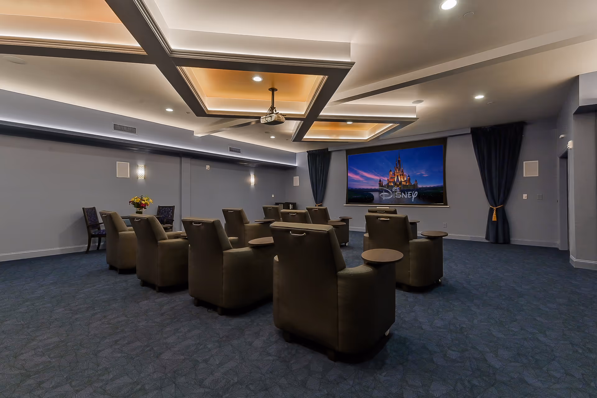 Cozy media room with recliner seats arranged facing a large screen displaying the Disney castle.