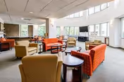 Bright senior-living lounge with colorful couches, round tables, and large windows.