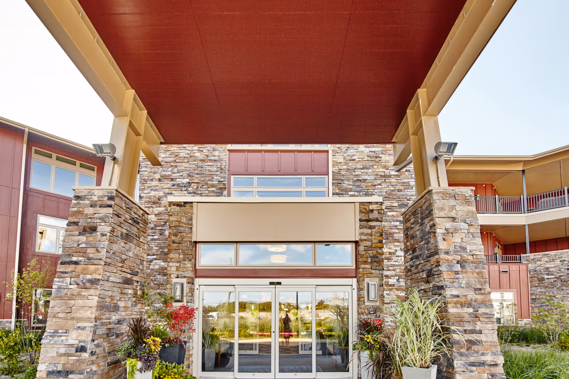 Entrance of The Summit facility with stone pillars, glass automatic sliding doors, and a covered canopy. There are plants and greenery around the entrance area.