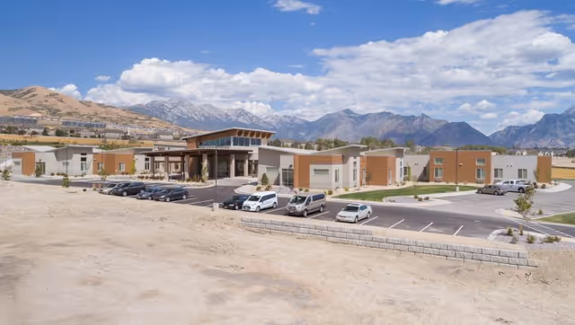 Front exterior of the Pointe Meadows senior living building with parked cars and mountains in the background.