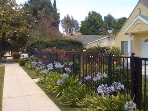 Exterior view of Golden Years III showing a sidewalk, garden beds, and a yellow building façade.