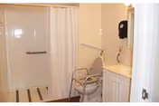 Bathroom with a walk-in shower featuring a white curtain, a shower chair with armrests, a grab bar on the wall, a sink with a countertop, and a soap dispenser mounted on the wall.