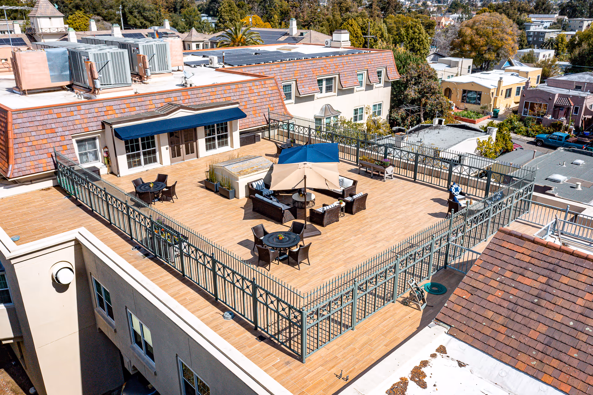 Rooftop terrace with wicker seating, umbrellas, dining tables, and decorative fencing overlooking neighboring buildings.