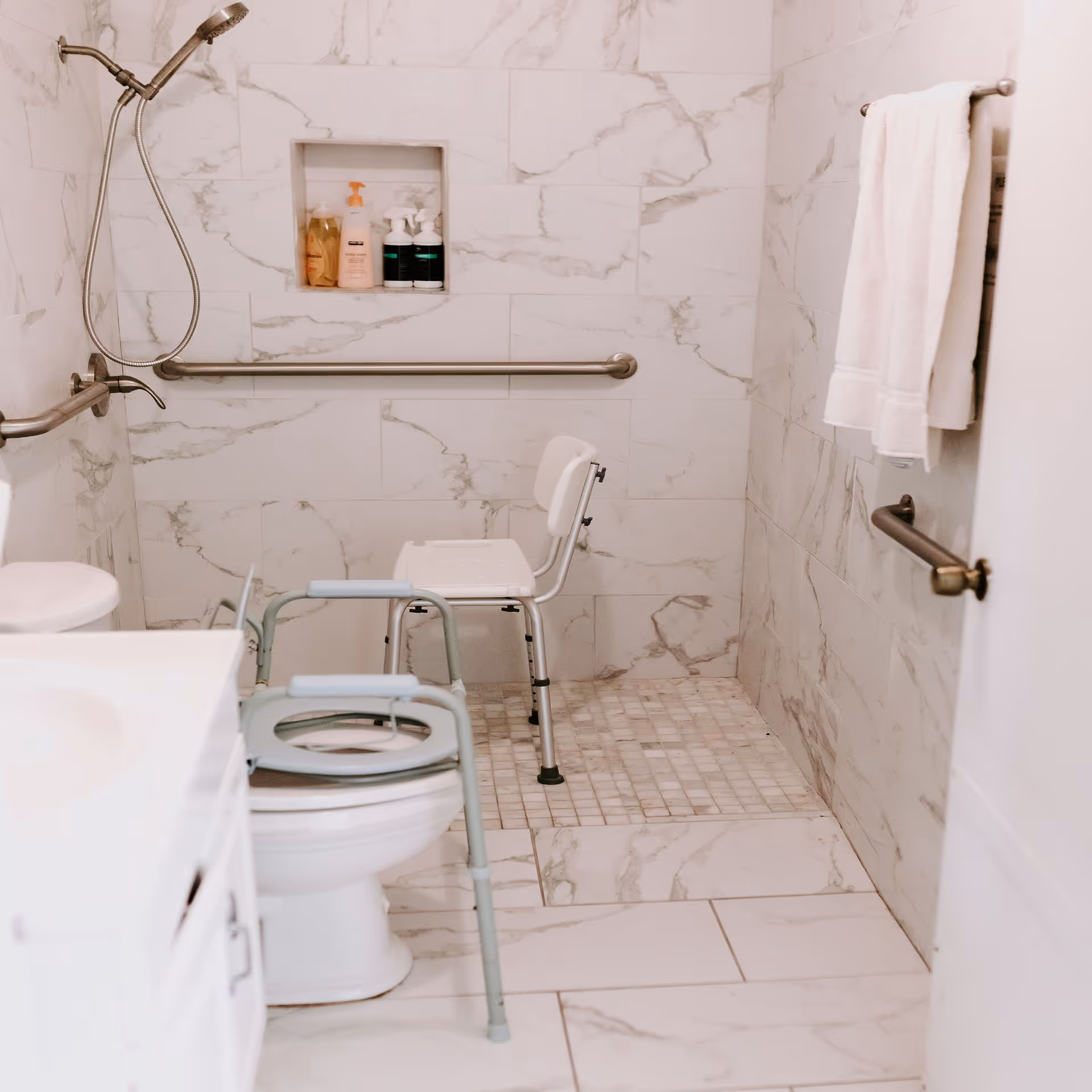 Accessible bathroom with a shower chair, grab bars, and marble tiling.