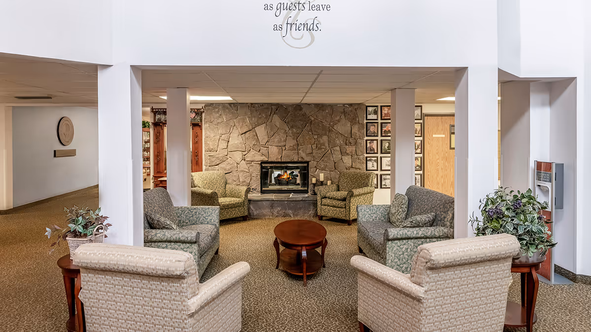 Seating area with upholstered chairs and sofas around a coffee table facing a stone fireplace in a senior living facility.