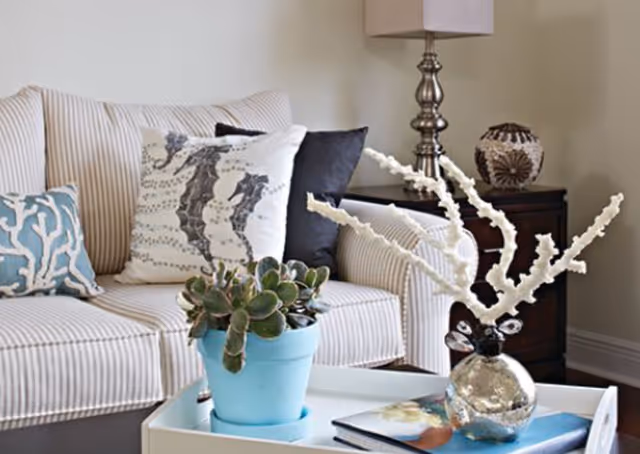 A striped sofa with coastal-themed pillows beside a side table and a coffee table holding a potted succulent and a decorative coral sculpture.