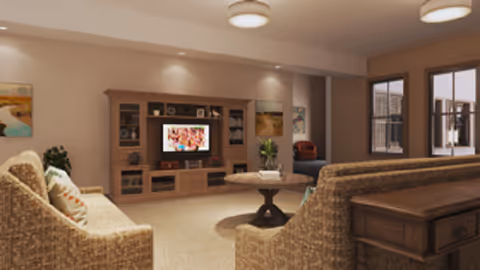 A cozy living room with two beige sofas facing a wooden entertainment center with a television. The room has soft lighting from ceiling fixtures and recessed lights. There are decorative paintings on the walls and a round wooden coffee table in the center. A window on the right side lets in natural light.