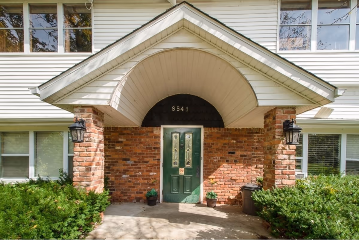 Brick building entrance with green door under arch and two brick columns with lanterns