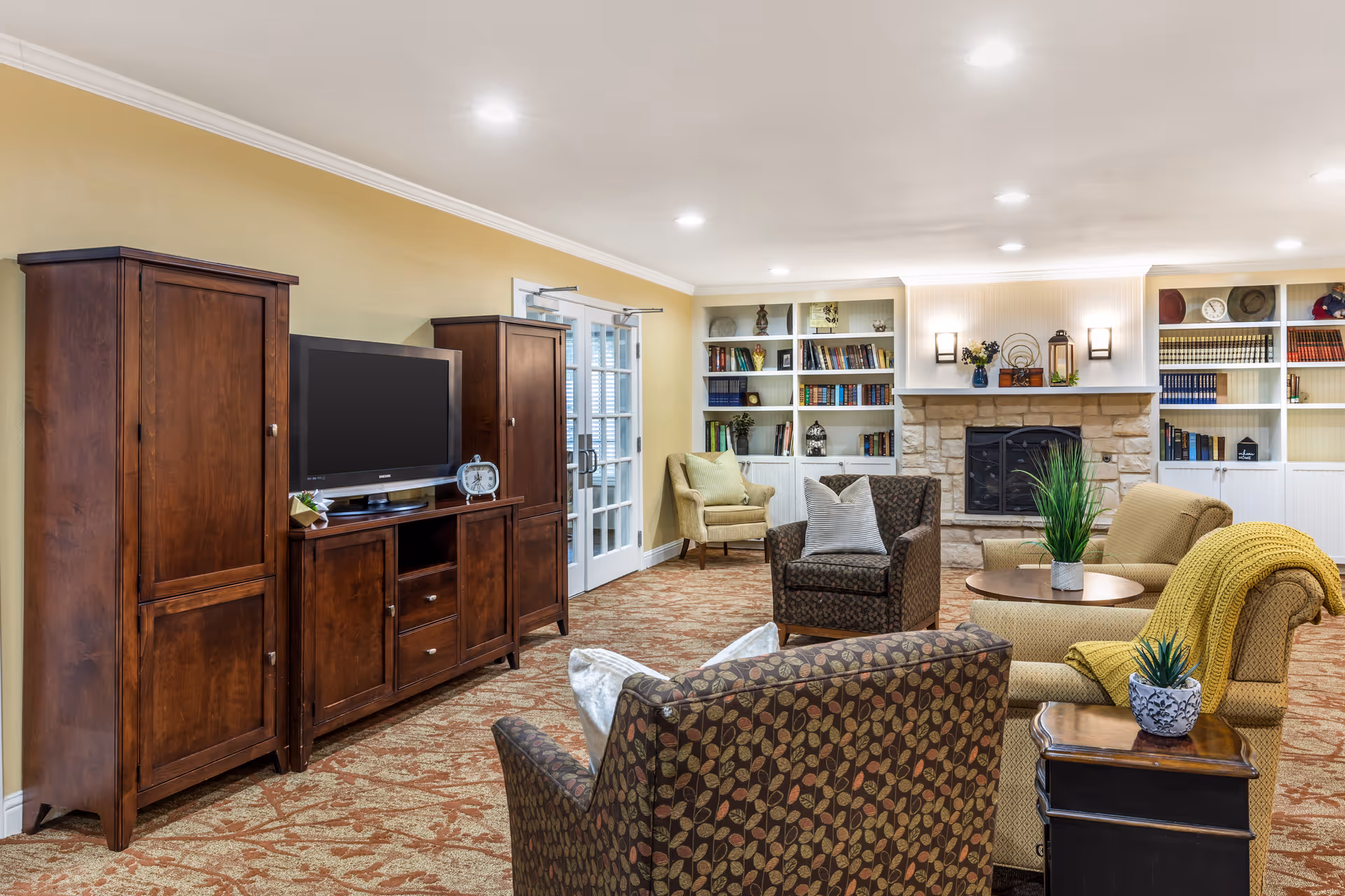 Cozy communal living room with armchairs, a TV cabinet, bookshelves and a fireplace.