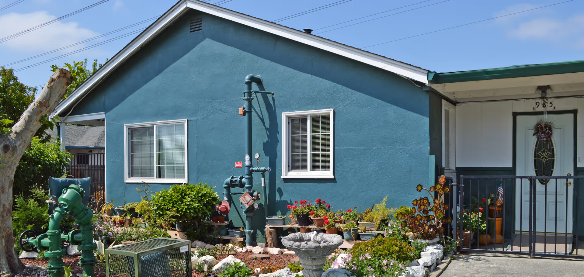 Front exterior of a teal single-story guest home with a small garden of potted plants and a gated porch entry.