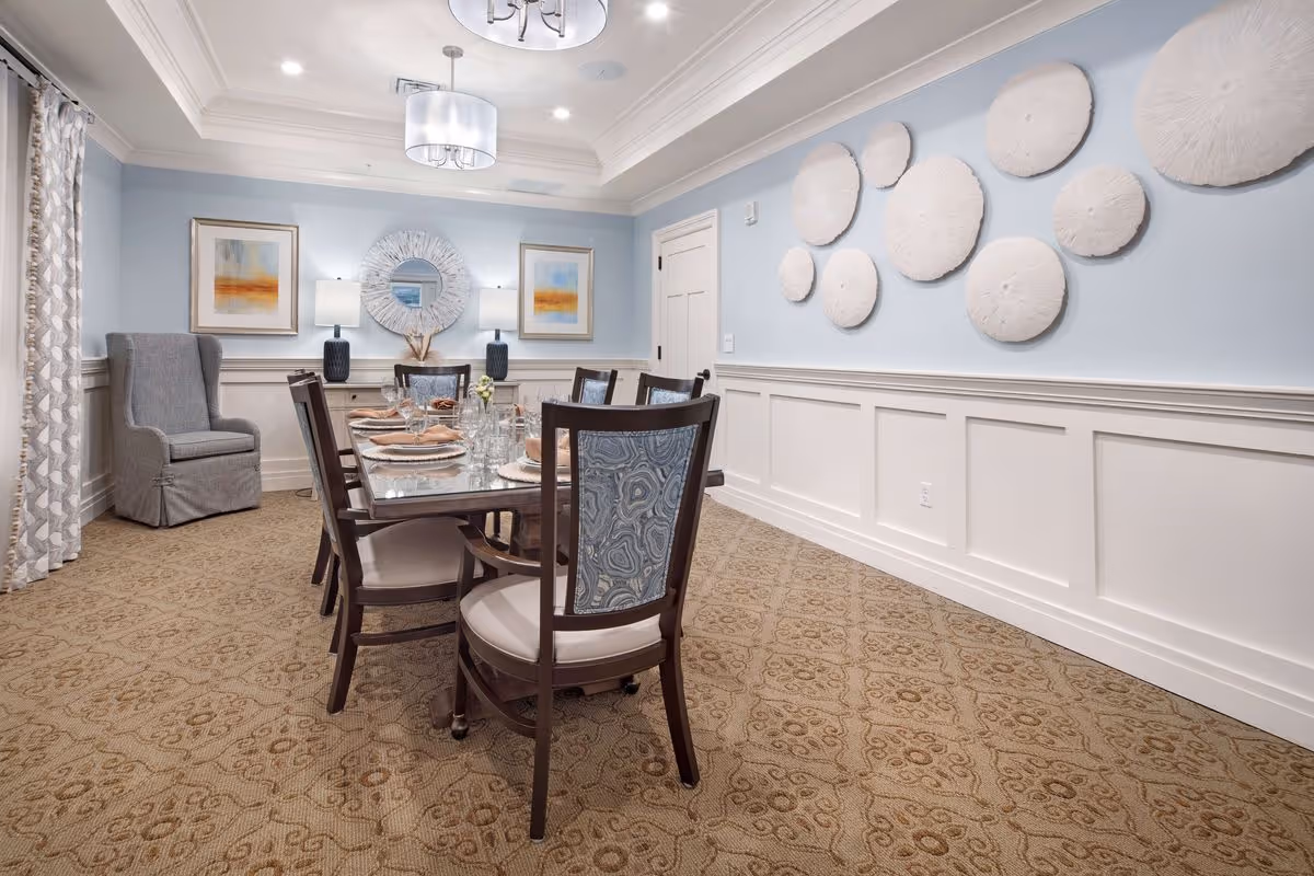 Well-appointed dining room with a glass-top table set for a meal, upholstered chairs, blue walls and decorative wall art.