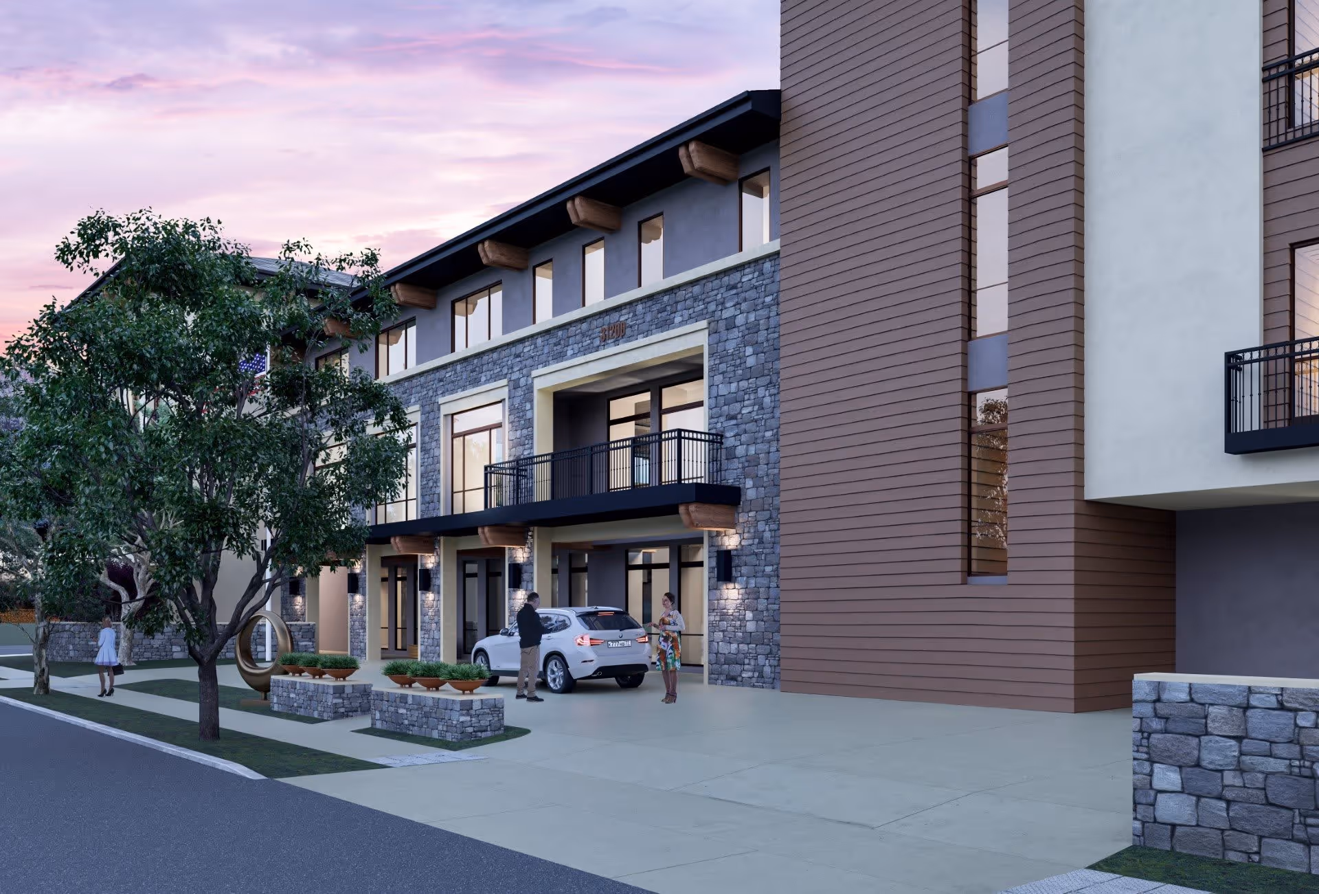 Entrance and facade of a multi-story senior living building with stone and wood exterior, a tree-lined driveway, a parked car and people near the entrance at dusk.