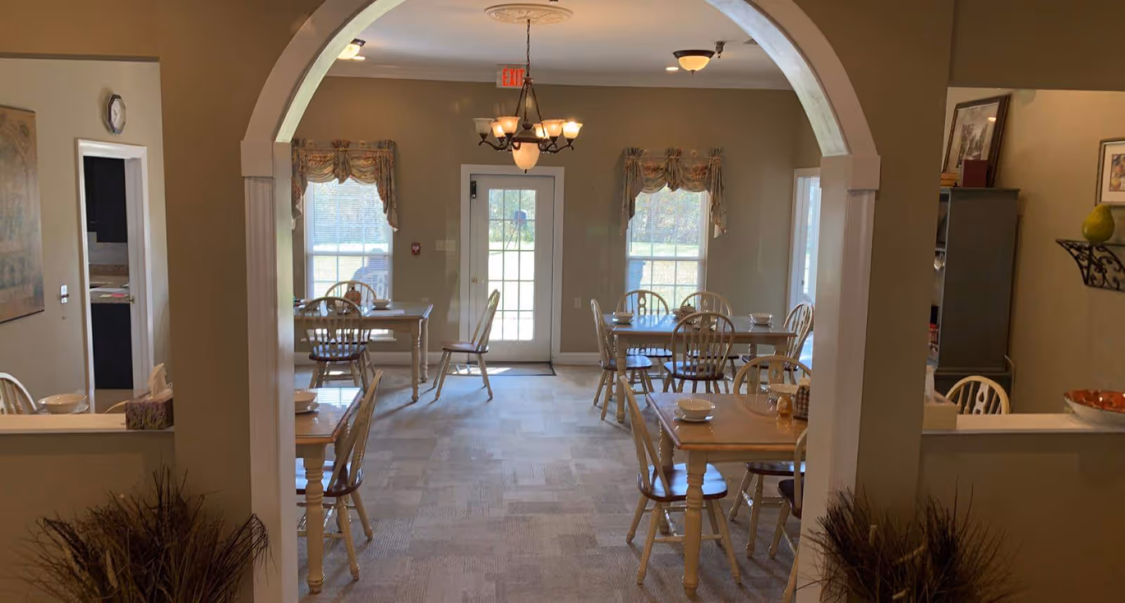 Dining room with several wooden tables and chairs under chandeliers seen through an arched entryway.
