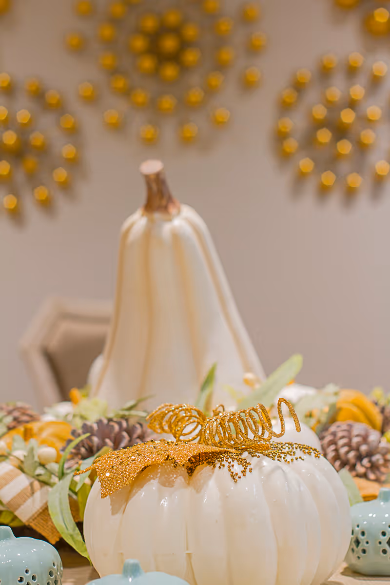 White decorative pumpkins with glitter and pinecones arranged as an autumn centerpiece on a table.