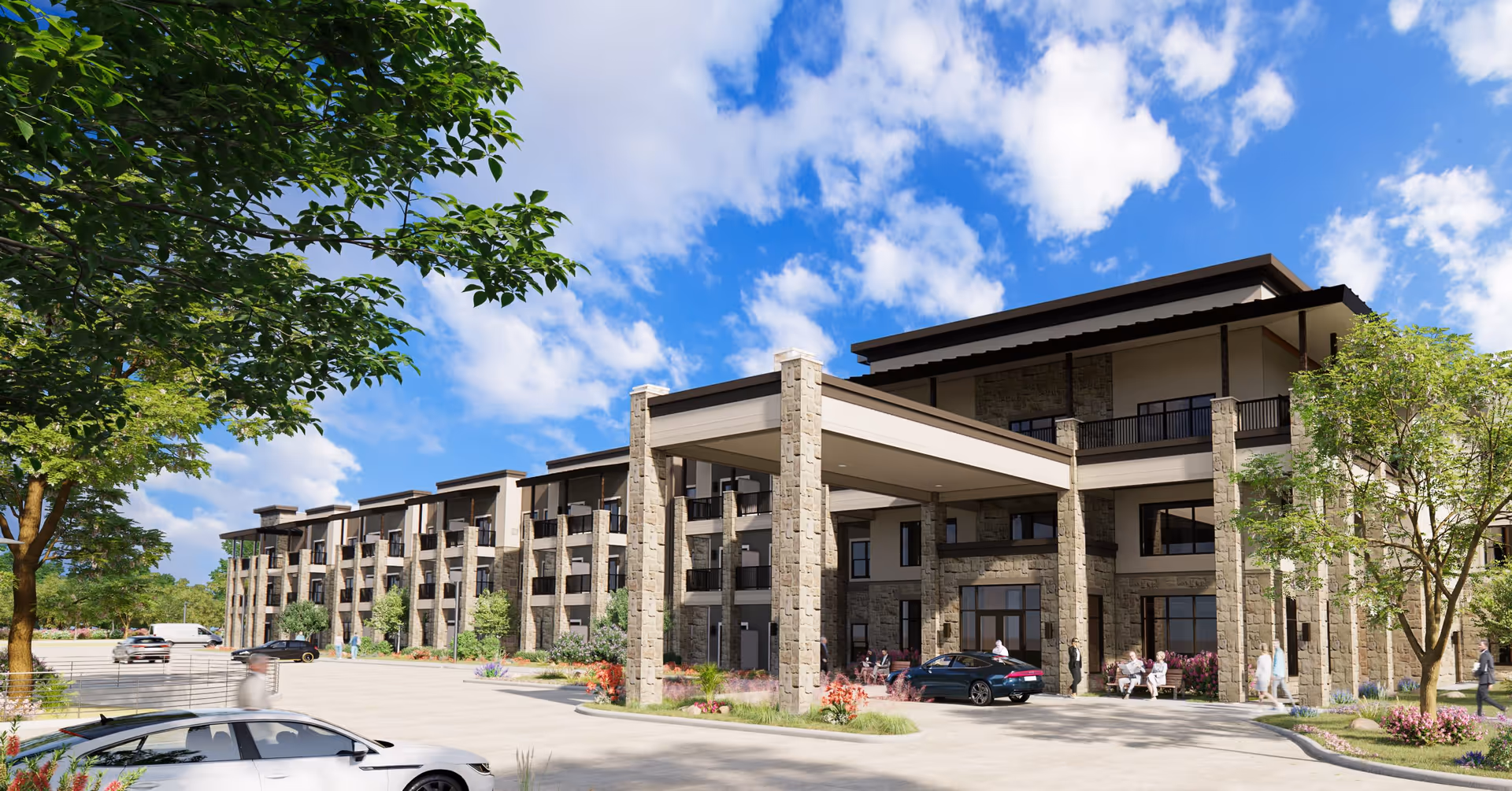 Exterior view of a modern senior living facility building with stone pillars and balconies under a blue sky with scattered clouds. Several people are walking or sitting near the entrance, and cars are parked in front of the building surrounded by landscaped greenery and trees.